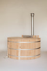 Cedar wood hot tub with a stainless steel chimney and a wooden lid, set against a neutral background.