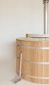 Cedar hot tub with a wooden lid and metal bands, featuring a metal scoop beside it.