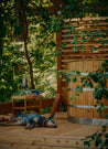 Cedar hot tub beside a wooden deck, with a dog resting nearby in a lush green setting.