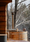 Person in a wooden hot tub with a snowy forest background