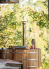 Wooden hot tub with steam rising, surrounded by trees