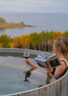 Woman reading a book and holding a glass of wine in a hot tub with a scenic view.