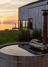 Outdoor hot tub with scenic view of a building and sunset over water.