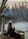 Person sitting in an outdoor hot tub with a view of a snowy forest.