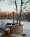 Wooden hot tub in a snowy outdoor setting with trees and sunset.