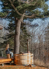 Two people in a wooden hot tub surrounded by trees and nature.