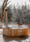 Person in a wooden hot tub surrounded by a snowy forest