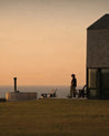 Person standing on a deck at sunset near a house with a view of the ocean.
