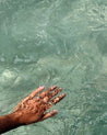 A hand submerged in clear water, creating ripples and bubbles, reflecting sunlight.