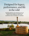 Cedar wood fired hot tub beside a river, featuring a stainless steel chimney and natural surroundings.