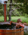 A wood burning cedar hot tub with smoke coming out of the chimney and a woman looking out from it at a forest
