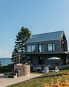 Modern house by the sea with people sitting on the grass and near a wood fired hot tub.