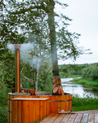 Woman in a wooden hot tub by a river with trees in the background