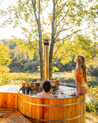 Two people in a cedar wooden hot tub surrounded by trees and nature.