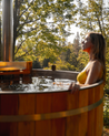 Woman in a yellow bikini sitting in a wood cedar hybrid hot tub surrounded by trees