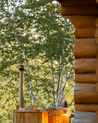 Person relaxing in a wooden hot tub with a log cabin and trees in the background