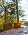 Person sitting in a cedar hot tub with a scenic view of trees and water.