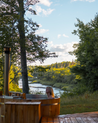 Person in a cedar wood hot tub surrounded by nature with trees and water in the background