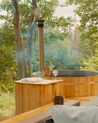 Cedar wood hot tub in a forest setting with trees and greenery.