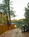 Person sitting on a wooden deck overlooking a scenic view with trees and water.