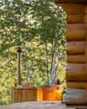 Person relaxing in a wooden hot tub with trees in the background