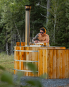 Man sitting in a wooden hot tub surrounded by trees