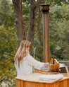 Cedar wood hot tub with woman opening the firebox lid next to a forest
