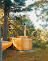 Wooden hot tub in a forest setting with trees and greenery.