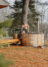 Man by a wooden hot tub in a forested area