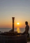 Person sitting in a hot tub watching the sunset over the ocean.