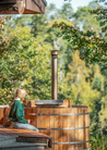 Person sitting on a wooden hot tub surrounded by trees