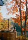 Person in a wooden hot tub surrounded by autumn trees with steam rising.