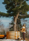 Person standing next to a wooden barrel in a snowy forest setting
