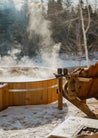 Wooden hot tub in a snowy outdoor setting with steam rising from it.