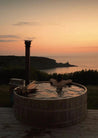 Person relaxing in a hot tub overlooking a scenic sunset over water.