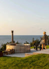 Person standing by a hot tub with ocean view at sunset