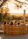 Group of people in a wooden hot tub at sunset