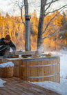 Wooden hot tub in a snowy outdoor setting with trees in the background