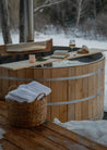 Wooden hot tub in a snowy outdoor setting with a basket and candle.