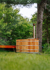 Wooden hot tub in a natural setting with trees and grass.