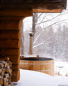 Wooden hot tub with a chimney in a snowy outdoor setting